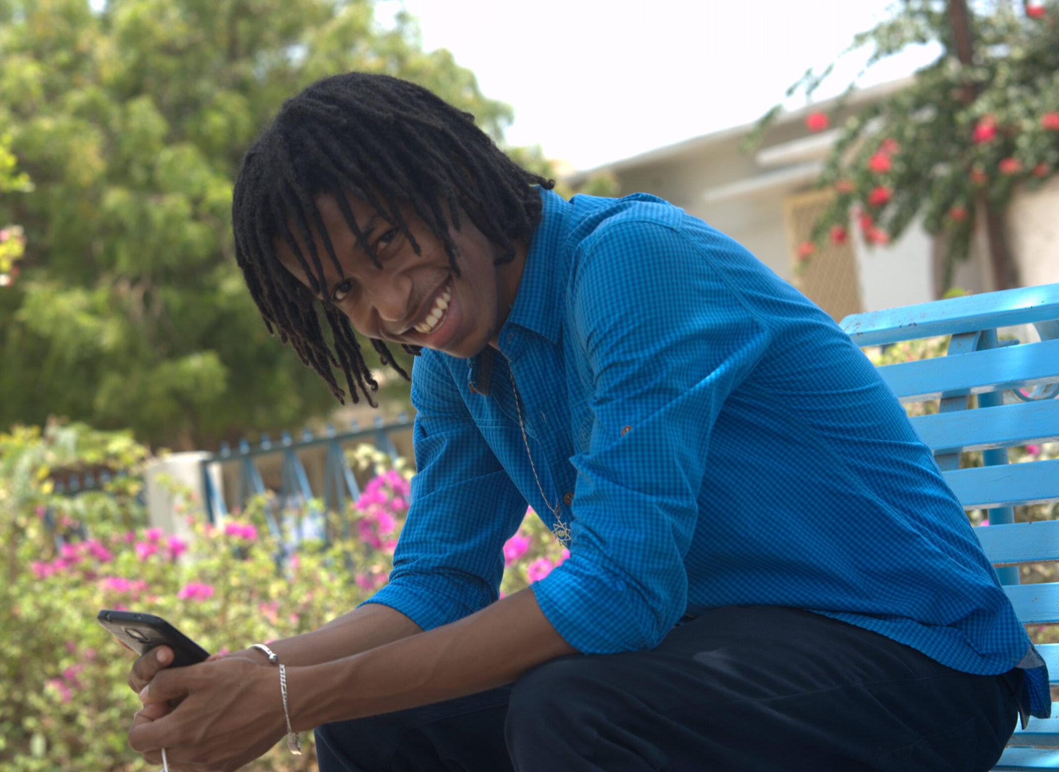 Male student in blue shirt in a garden background.