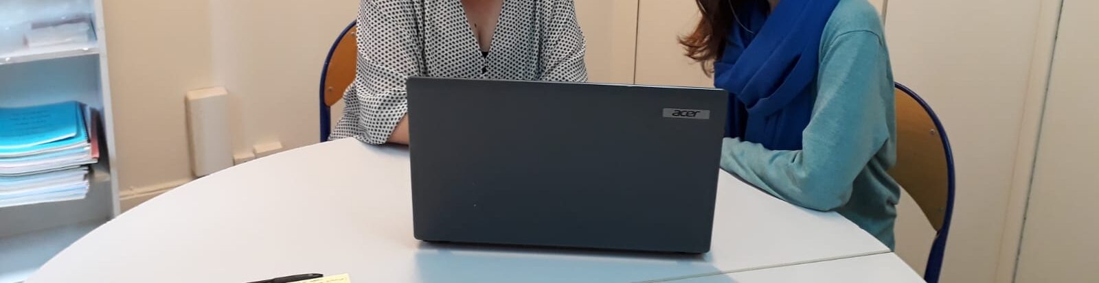 two women sitting behind a desk sharing a computer