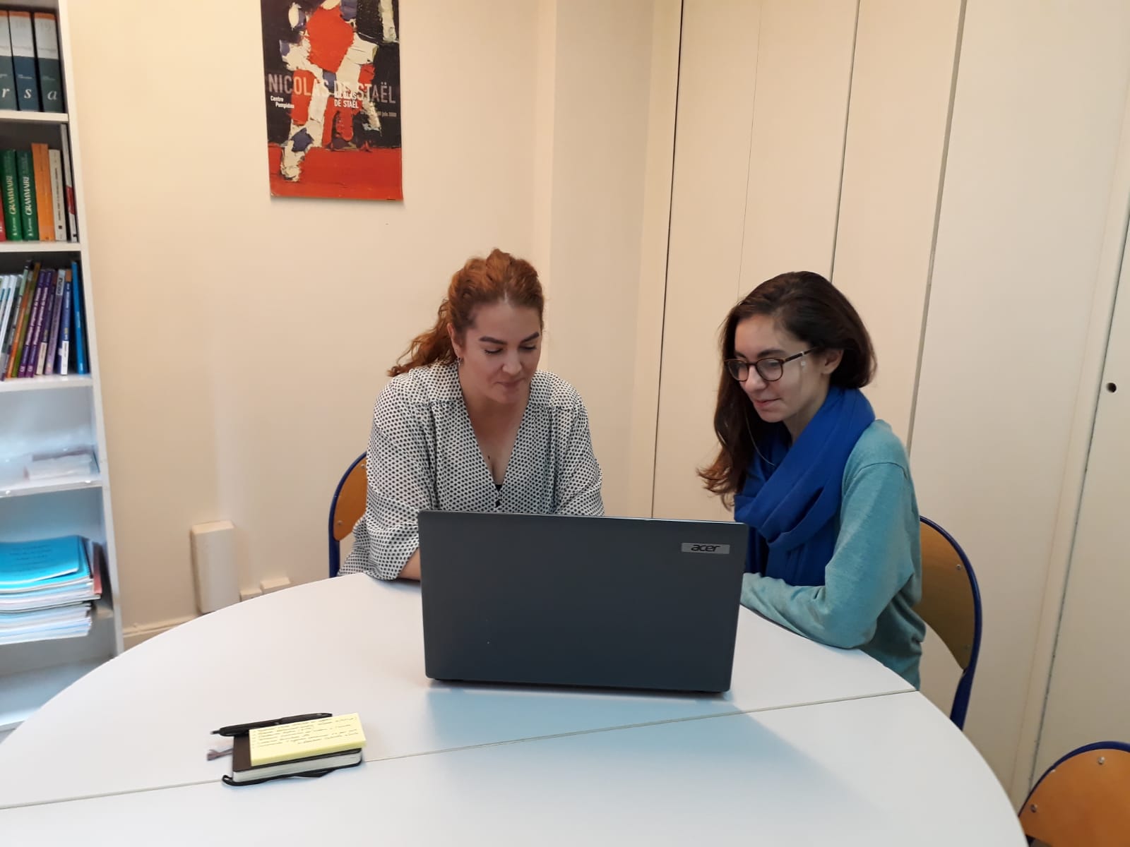 two women sitting behind a desk sharing a computer