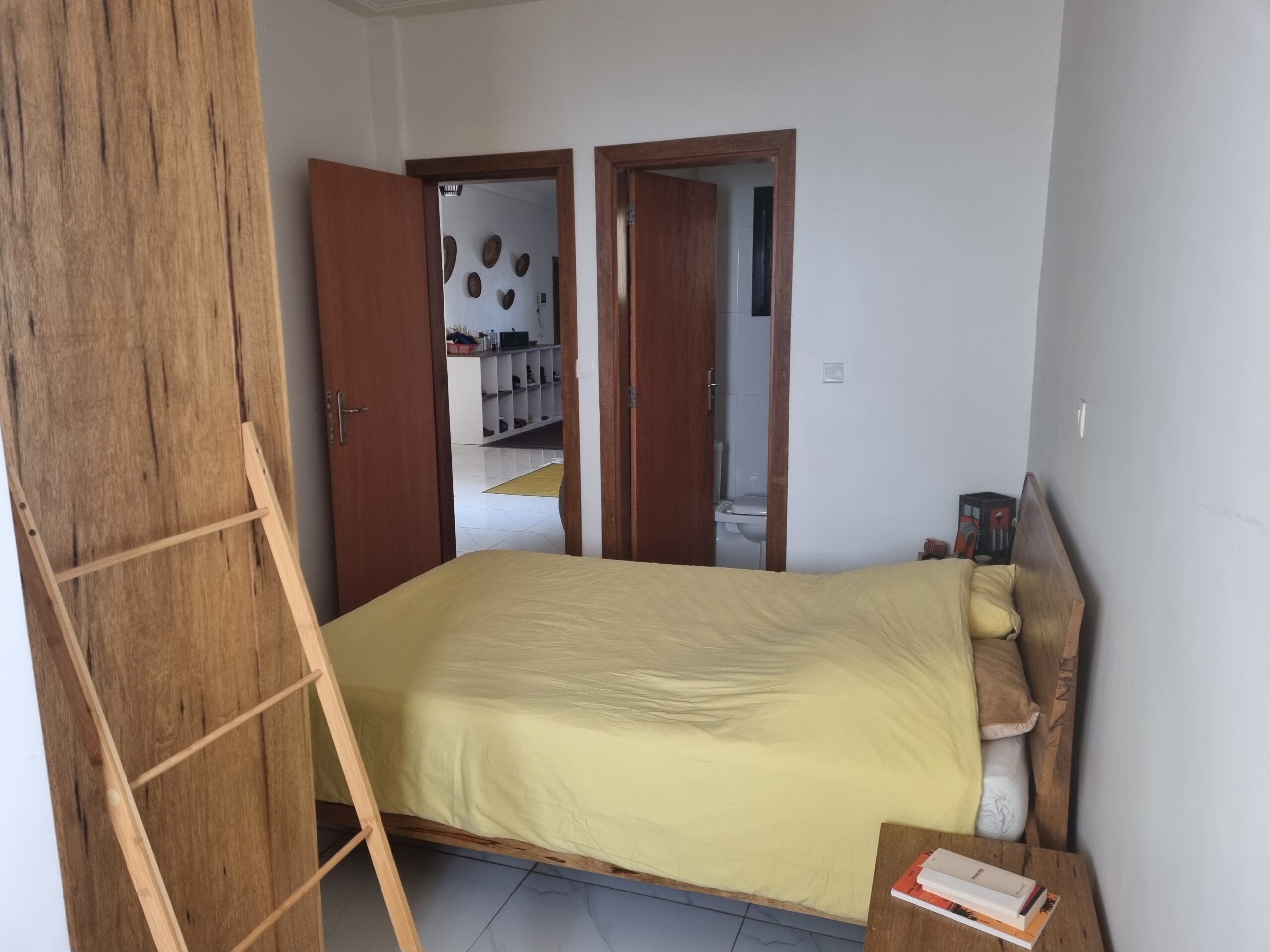 Bedroom has a bed with yellow bedspread, side table, door to bathroom and door to hallway.
