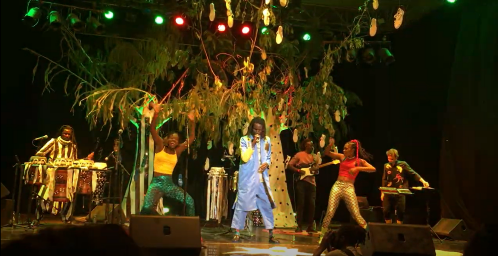 Singer and two backup dancers in front of faux trees on a stage