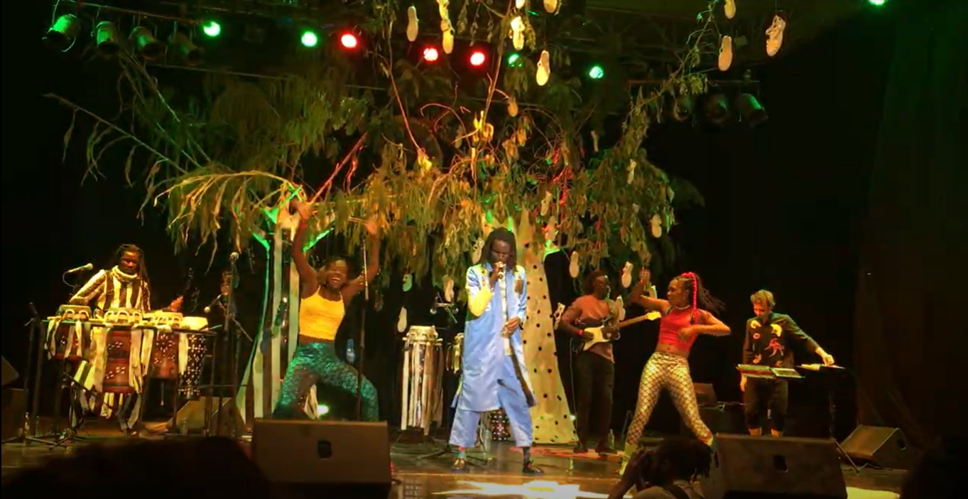 Singer and two backup dancers in front of faux trees on a stage
