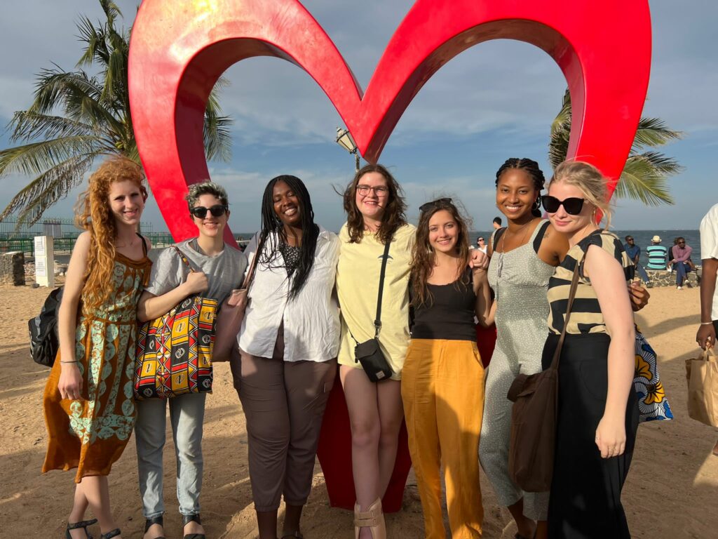 A group of seven smiling young women in front of a sculpture of a heart