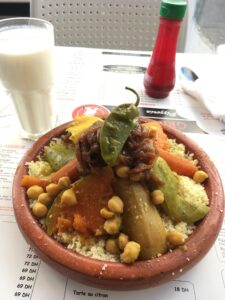 A clay dish of cooked vegetables and chickpeas arranged on top of couscous