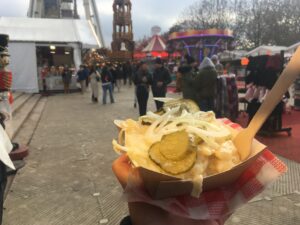 A cardboard container of potatoes, cheese, pickles, and onions