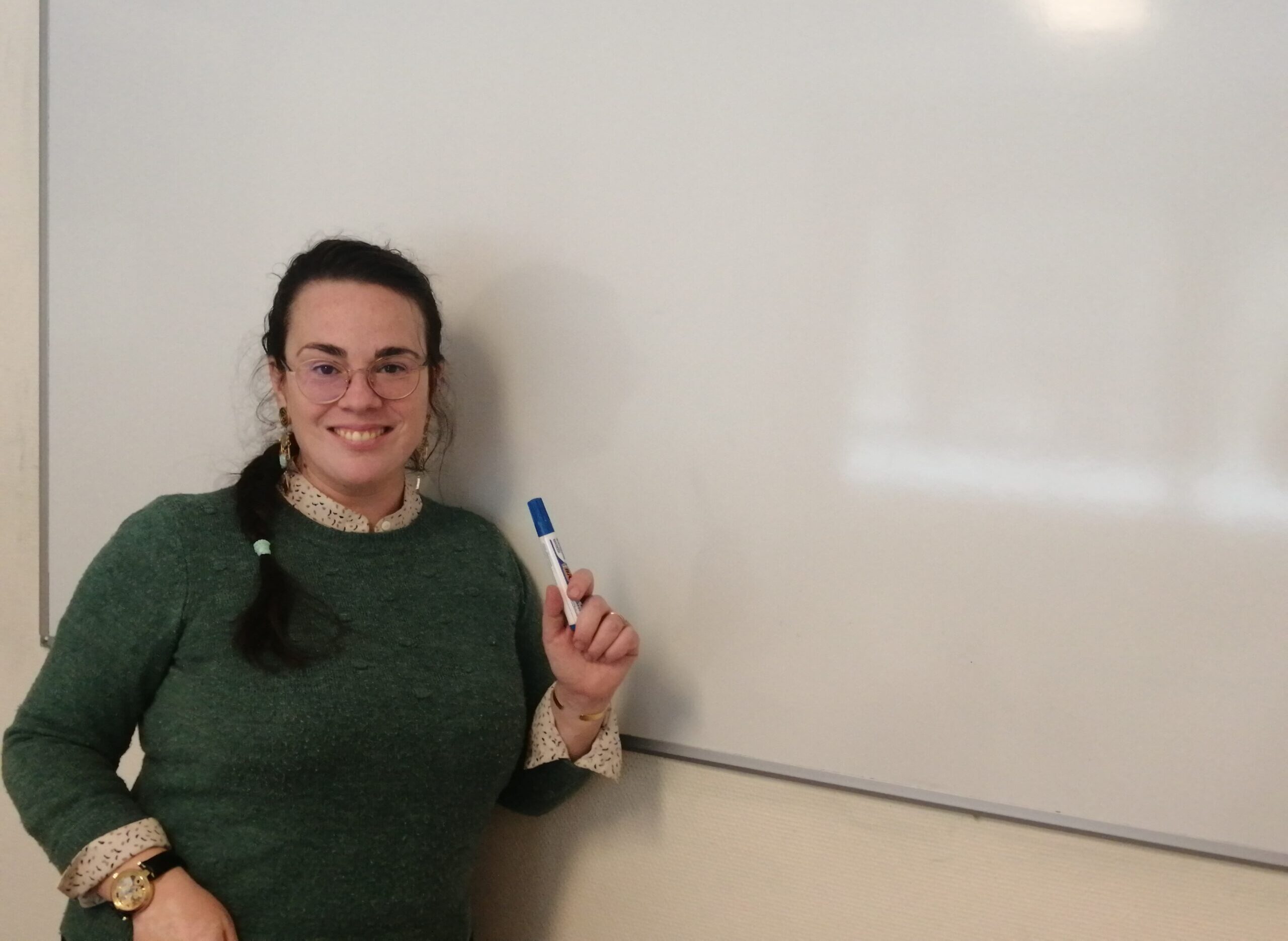 Female with glasses standing in front of a white board in a classroom